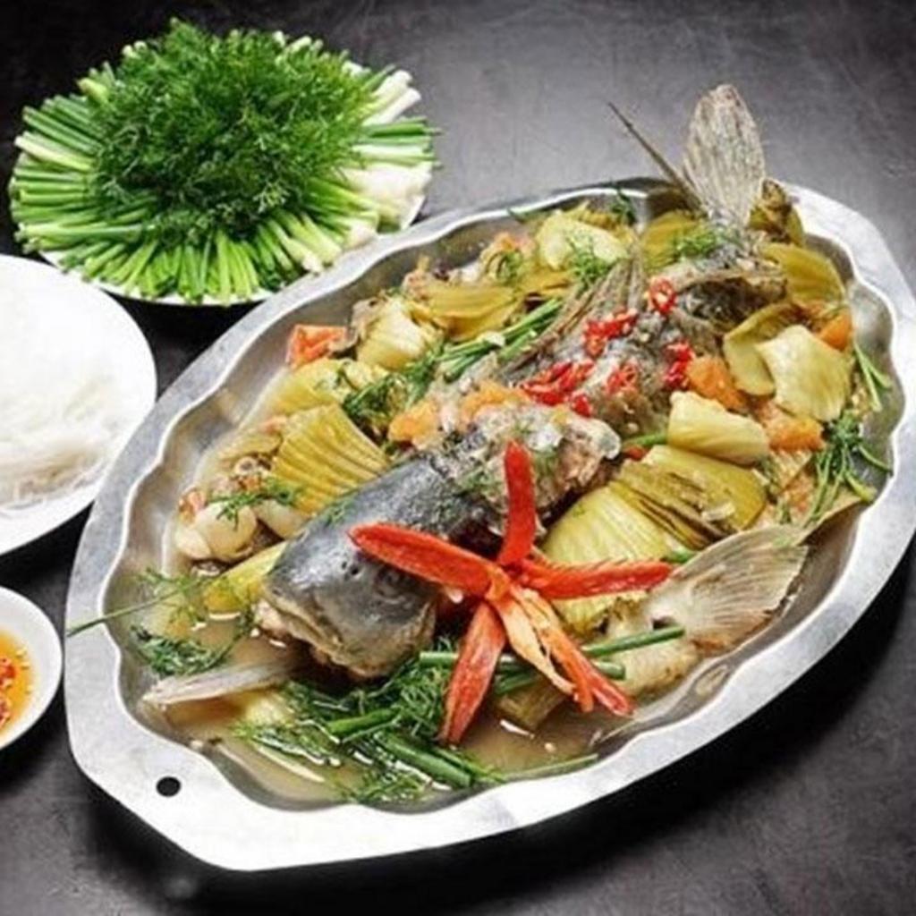 Đầu bếp sử dụng kẹp chuyên dụng để nhấc khay hấp nóng ra khỏi nồi một cách an toàn.